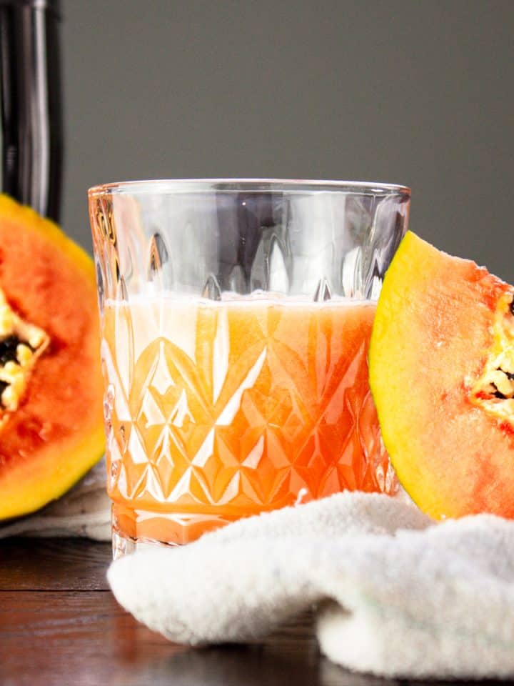 Glass of papaya rum punch beside half a papaya and a papaya slice
