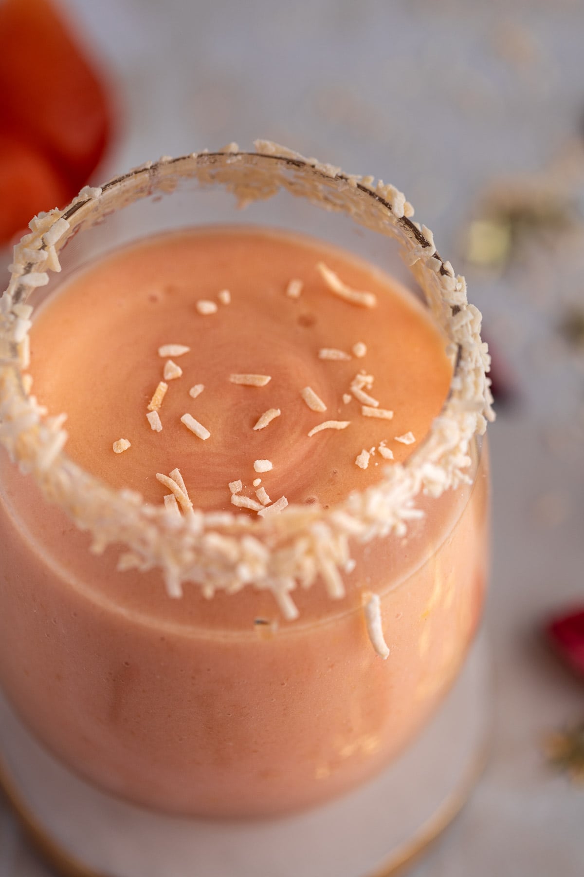 Up close view of the smoothie topped with shredded coconut, sitting on a white marble coaster.