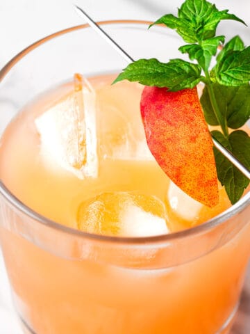 A peach on the beach cocktail garnished with a slice of peach and mint sprig.