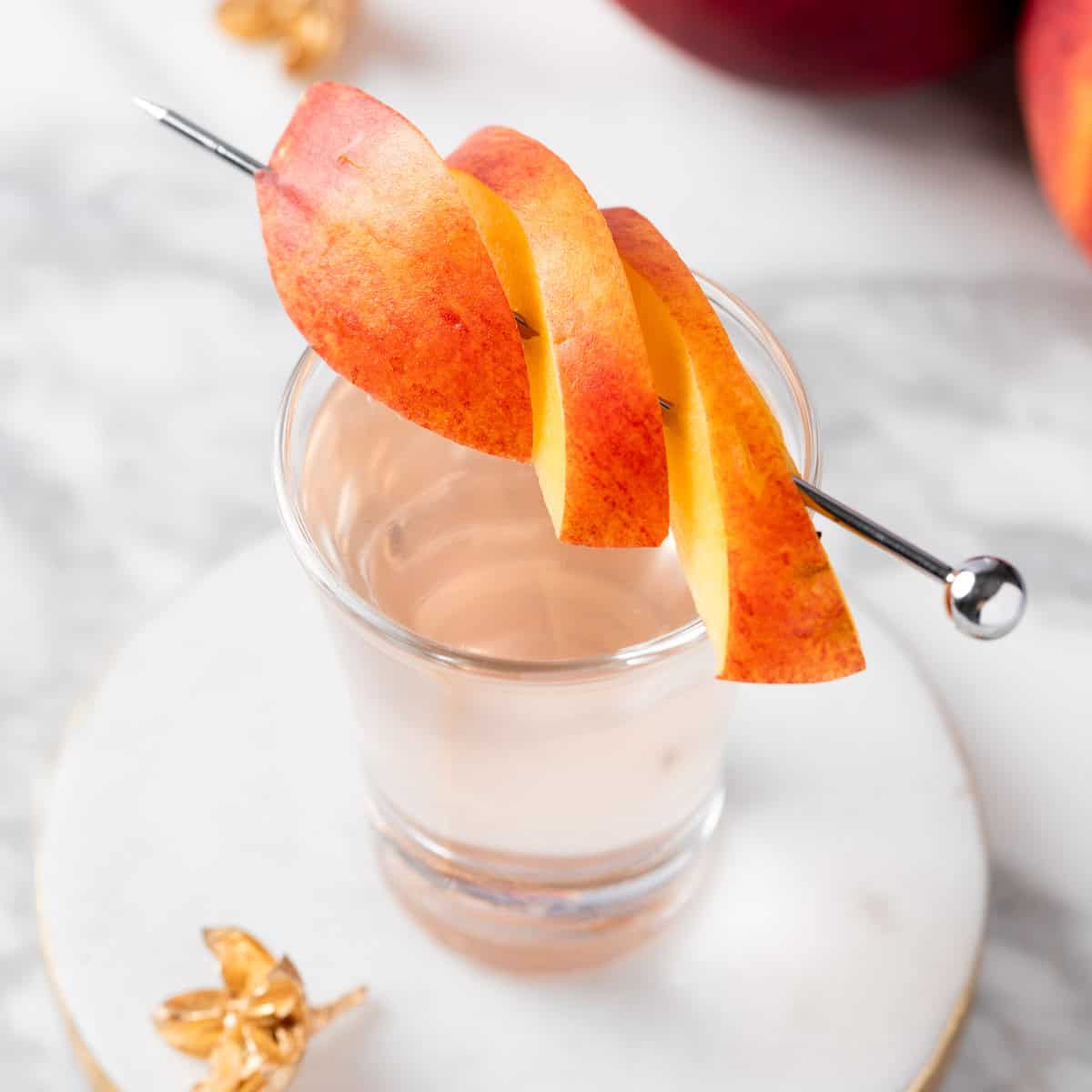 A peach vodka shot garnished with fresh peach slices.