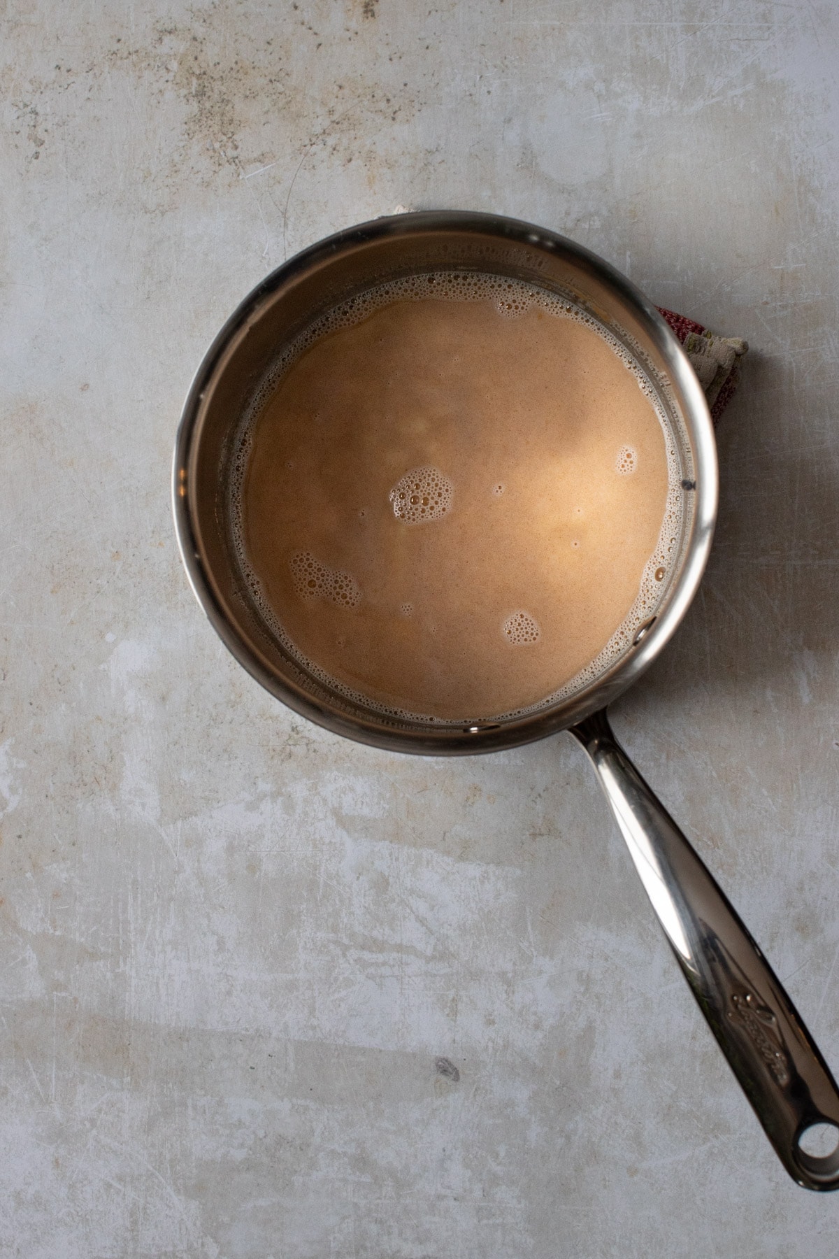 Overhead view of hot milk and peanut butter in a saucepan on warm marble background.