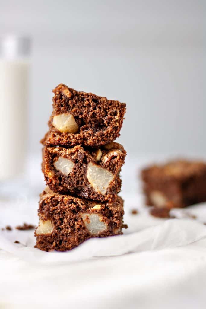 Three pear and hazelnut brownies stacked on top of each other, sitting on parchment paper