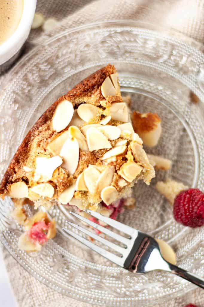 Overhead view of a half eaten piece of pear and raspberry cake on a glass plate next to a fork