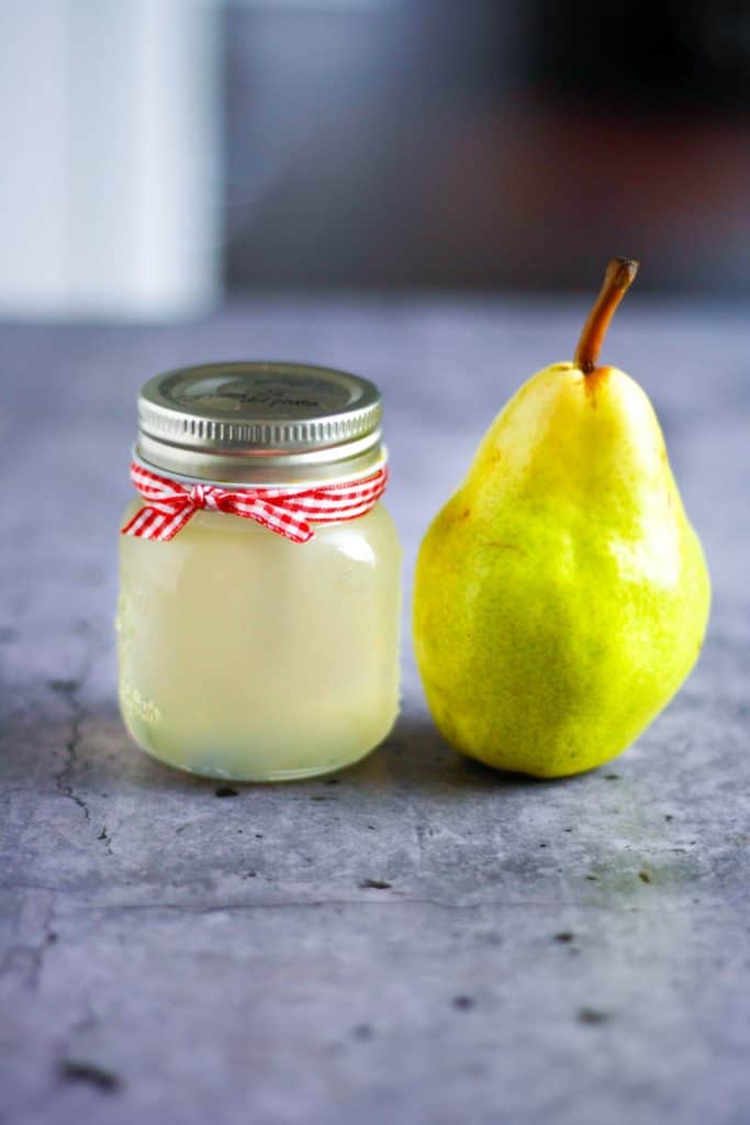 jar of pear simple syrup on table with pear lined up beside it