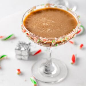 A peppermint espresso martini with a candy cane rim, on a round white marble board.