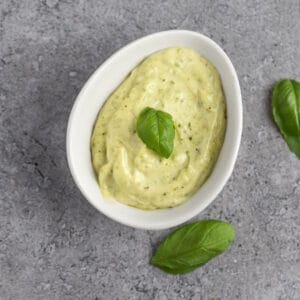 Pesto aioli garnished with fresh basil leaves, on a grey marble table.