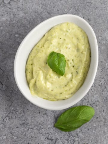 Pesto aioli garnished with fresh basil leaves, on a grey marble table.