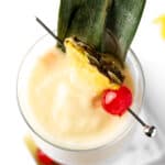 Overhead view of a pina colada with coconut milk, garnished with a pineapple slice and a maraschino cherry.