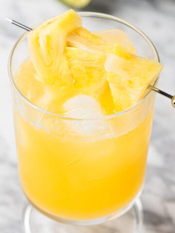 A pineapple gin cocktail garnished with fresh pineapple slices.