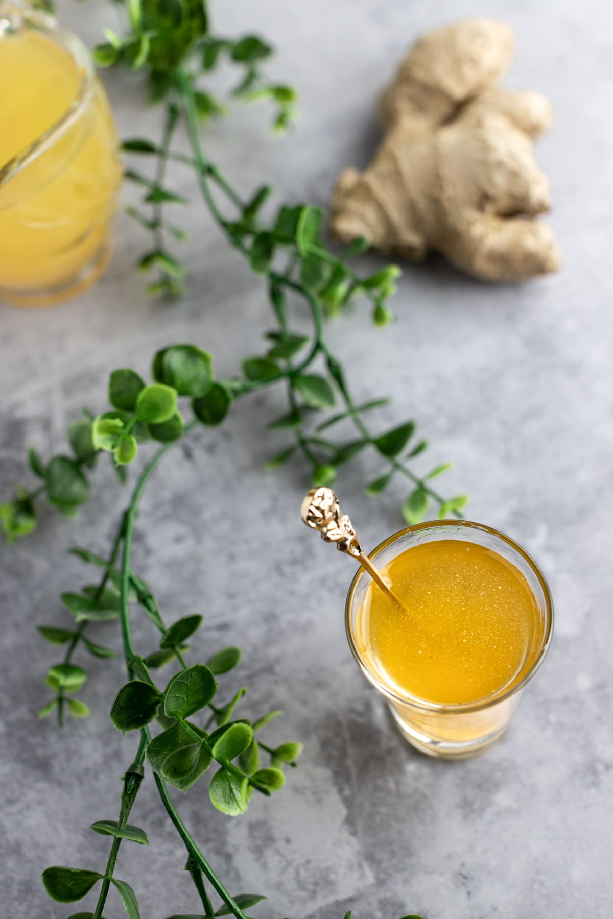 Overhead shot of ginger pineapple syrup on a grey background, next to green leaves and fresh ginger.
