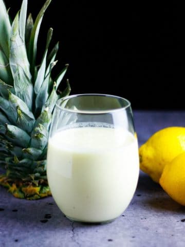 Glass of pineapple lemonade smoothie on the table with a pineapple top and lemons beside it