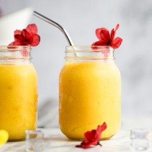 Two pineapple mango smoothies in jars with red flowers as decoration.