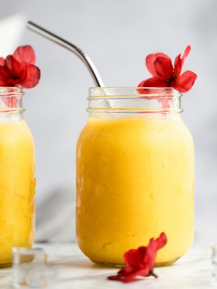 Two pineapple mango smoothies in jars with red flowers as decoration.