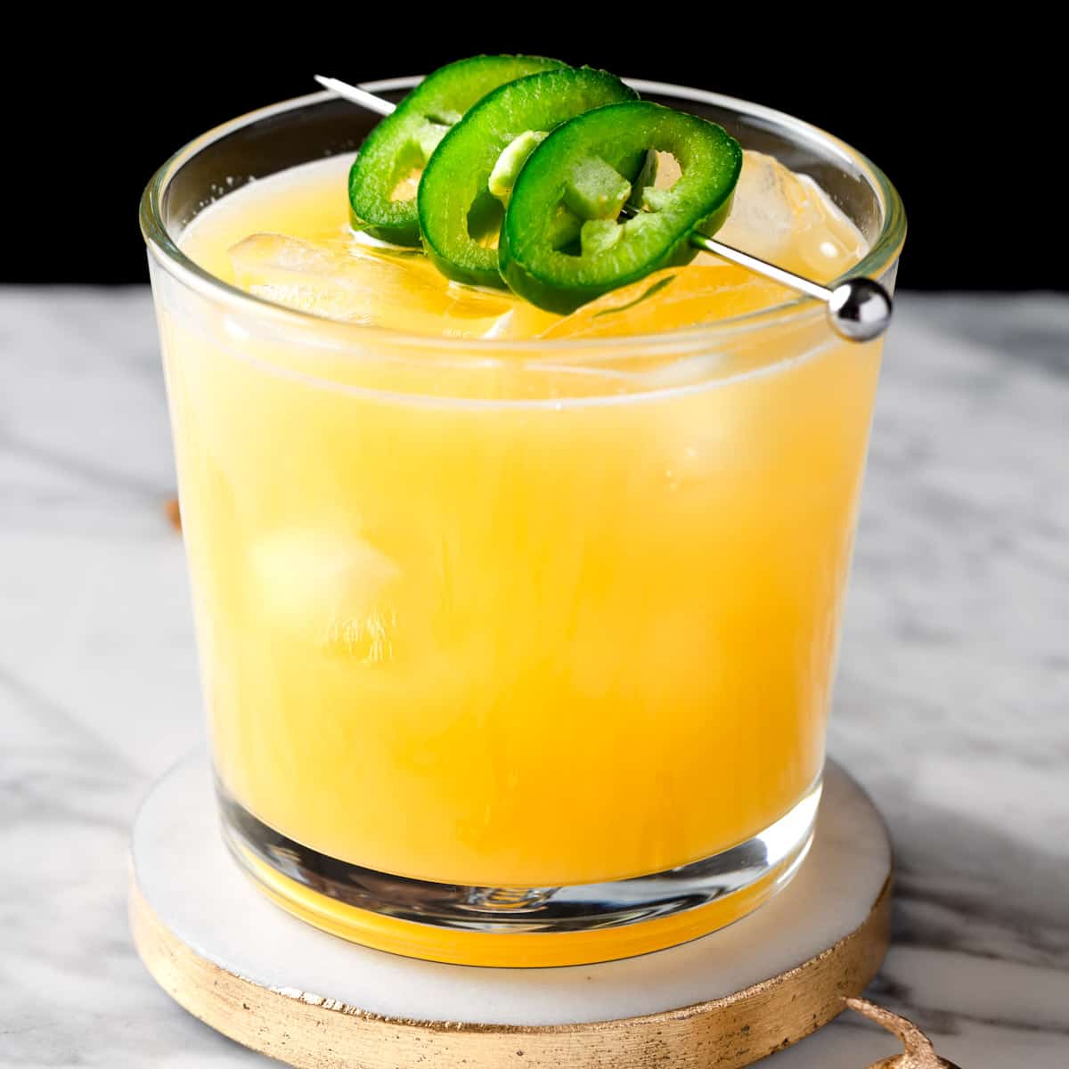 A pineapple mezcal cocktail garnished with jalapeno slices.