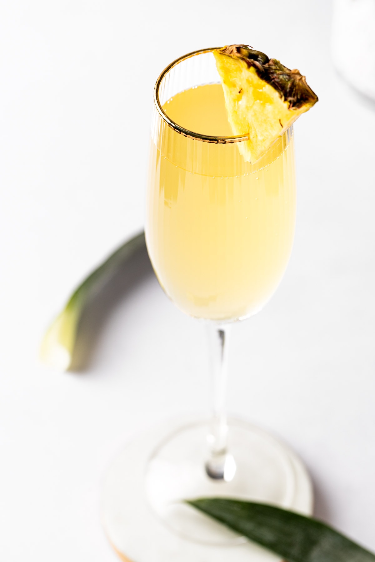 A pineapple mimosa in a champagne flute, garnished with a pineapple slice.