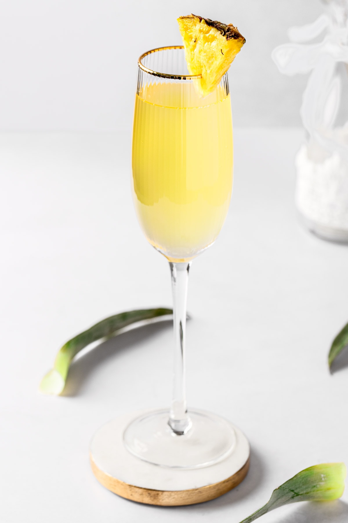 A pineapple mimosa garnished with a pineapple slice, on a white background.