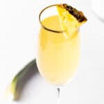A pineapple mimosa in a champagne flute, garnished with a pineapple slice.