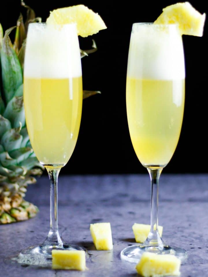 Two champagne glasses of pineapple mimosa on a table with a pineapple in the background