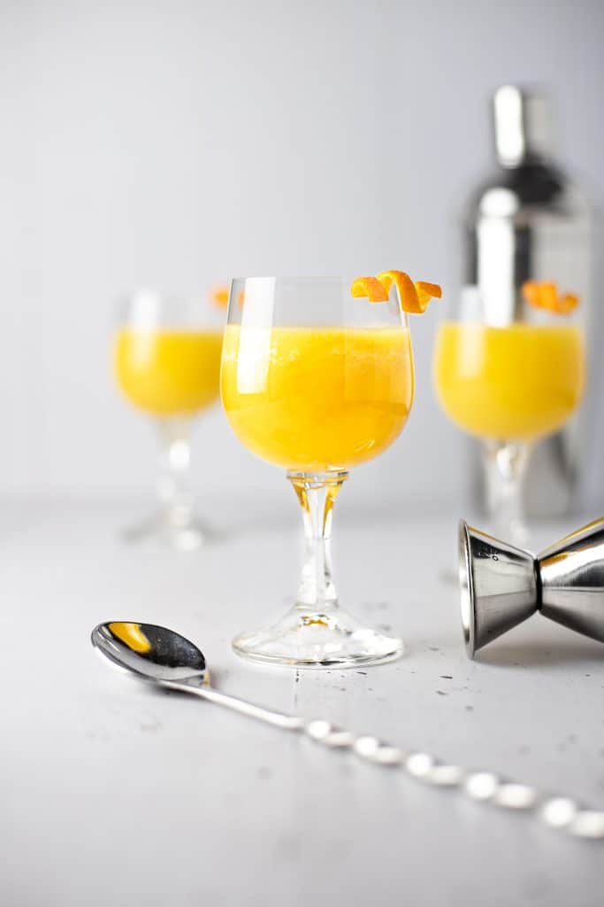 Three pineapple old fashioned cocktails with a metal spoon in front and cocktail shaker in the background