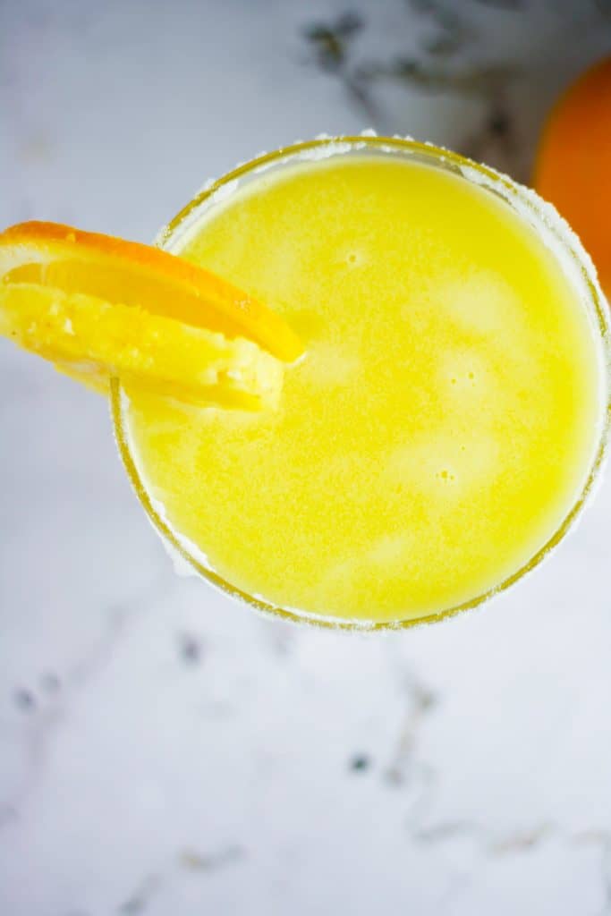 Overhead view of a glass of pineapple and orange margarita with orange and pineapple slices and sugar on the rim