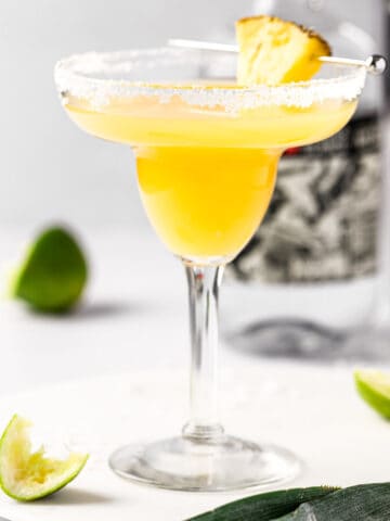A pineapple orange margarita with a salted rim, on a white marble table.