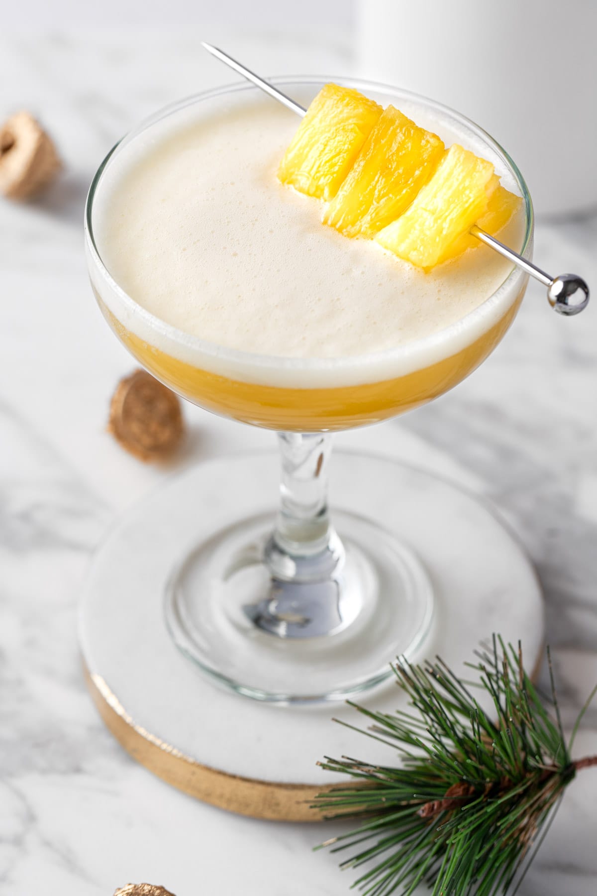 A pineapple whiskey sour garnished with pineapple chunks.