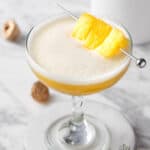 A pineapple whiskey sour garnished with pineapple chunks.