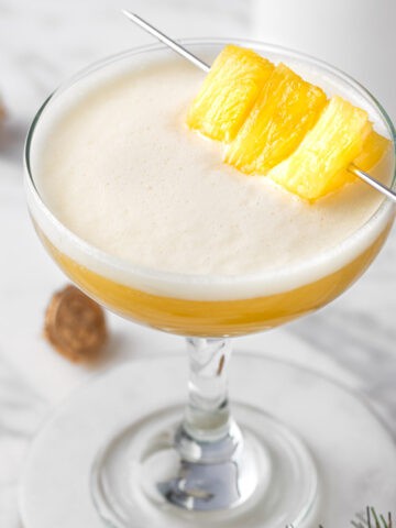 A pineapple whiskey sour garnished with pineapple chunks.