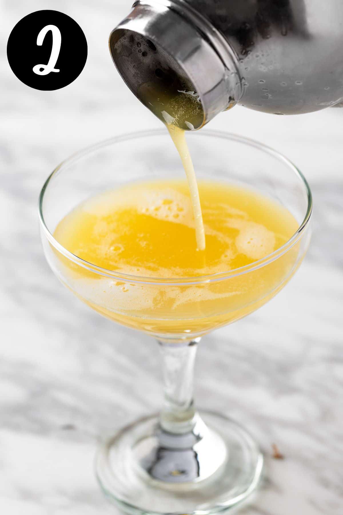 Pouring the whiskey sour from a cocktail shaker into a cocktail glass.