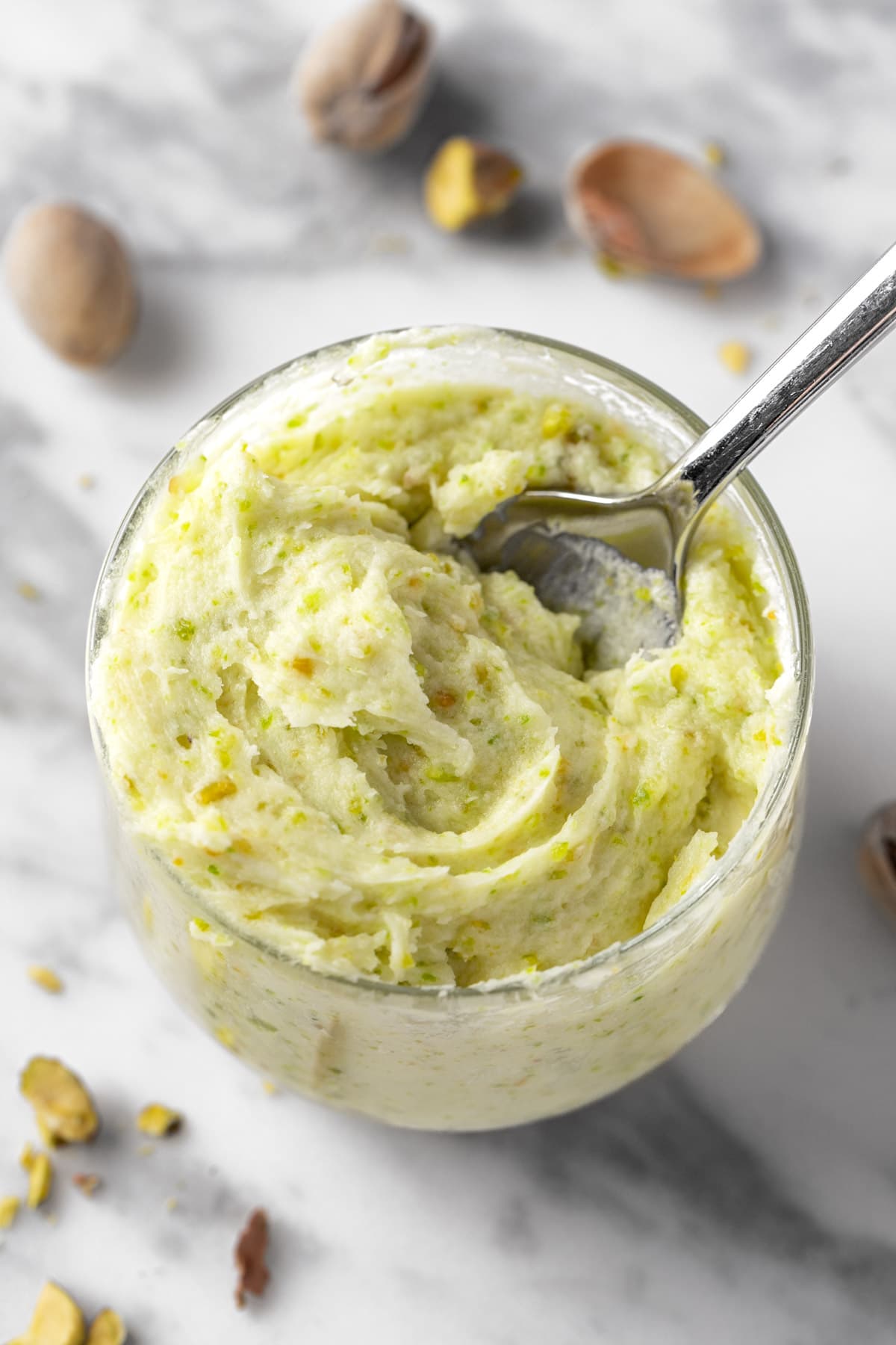 A small bowl of pistachio buttercream on a white marble table.