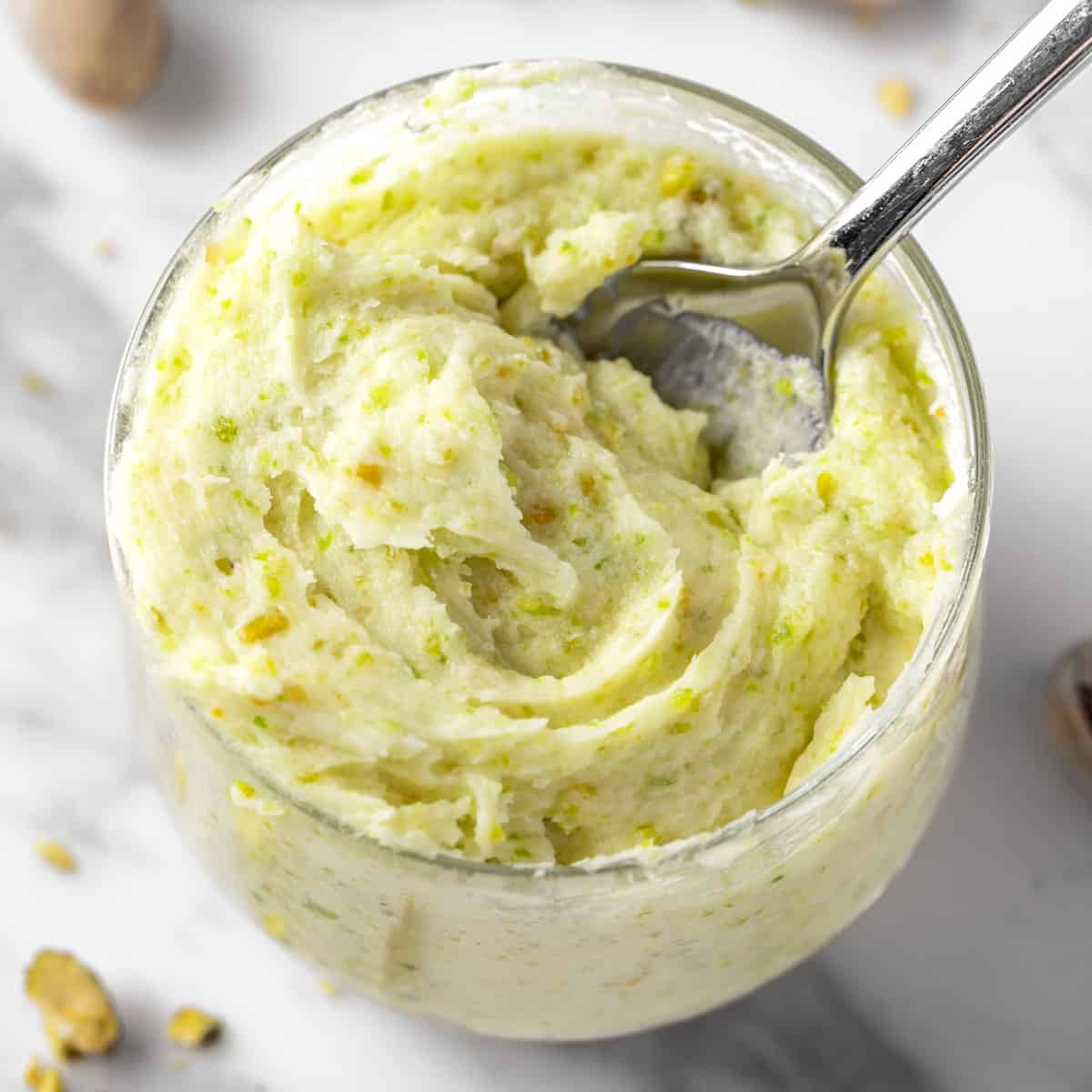 A bowl of pistachio buttercream on a white marble table. 