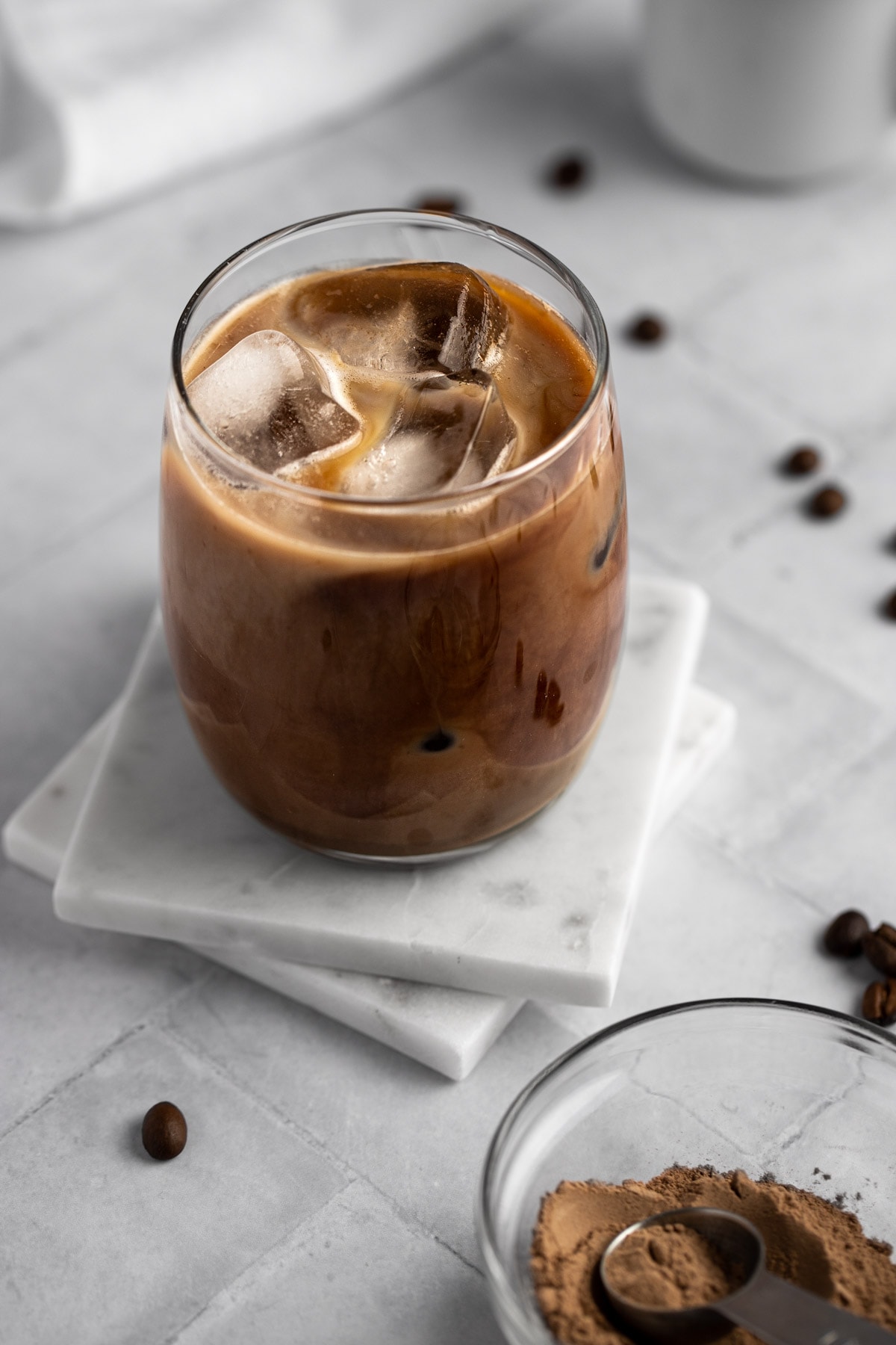 Overhead view of a glass of protein iced coffee sitting on two square white marble coasters.