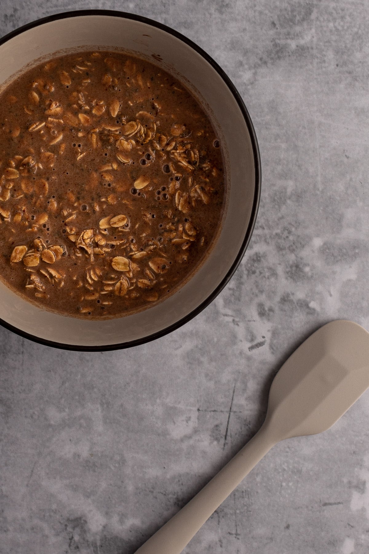 Overhead view of a liquid mixture of oats, milk, peanut butter and nutella, on a grey speckled background.