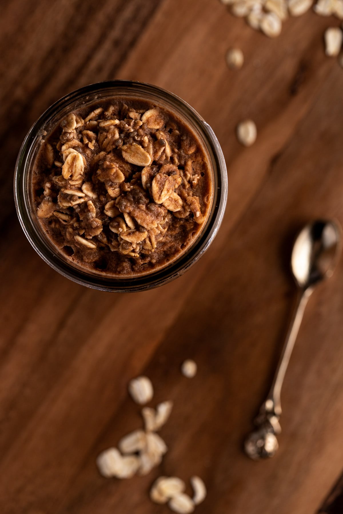 Overhead view of protein oats on a wooden board next to scattered oats and a small gold spoon.