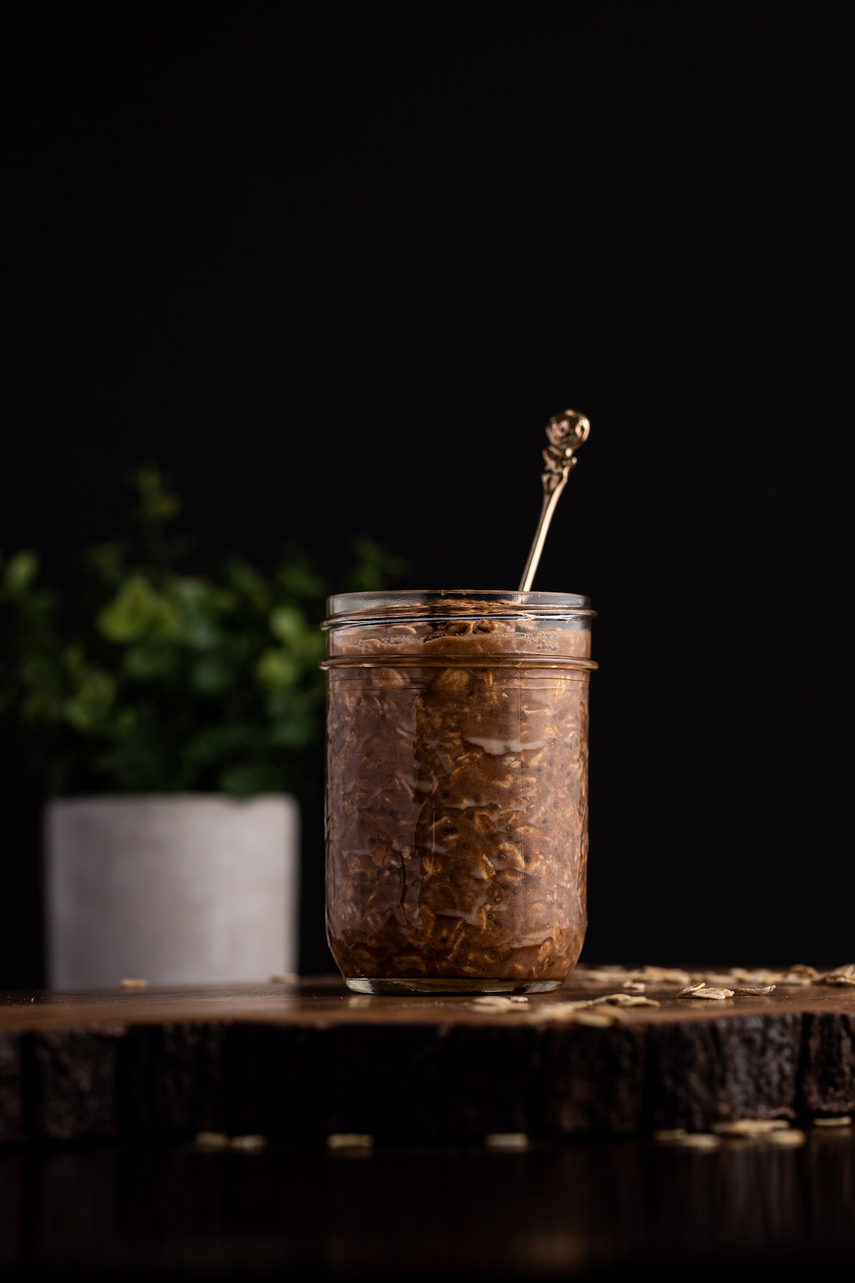 Protein overnight oats in a jar with a small gold spoon sticking out, a green plant in the background.