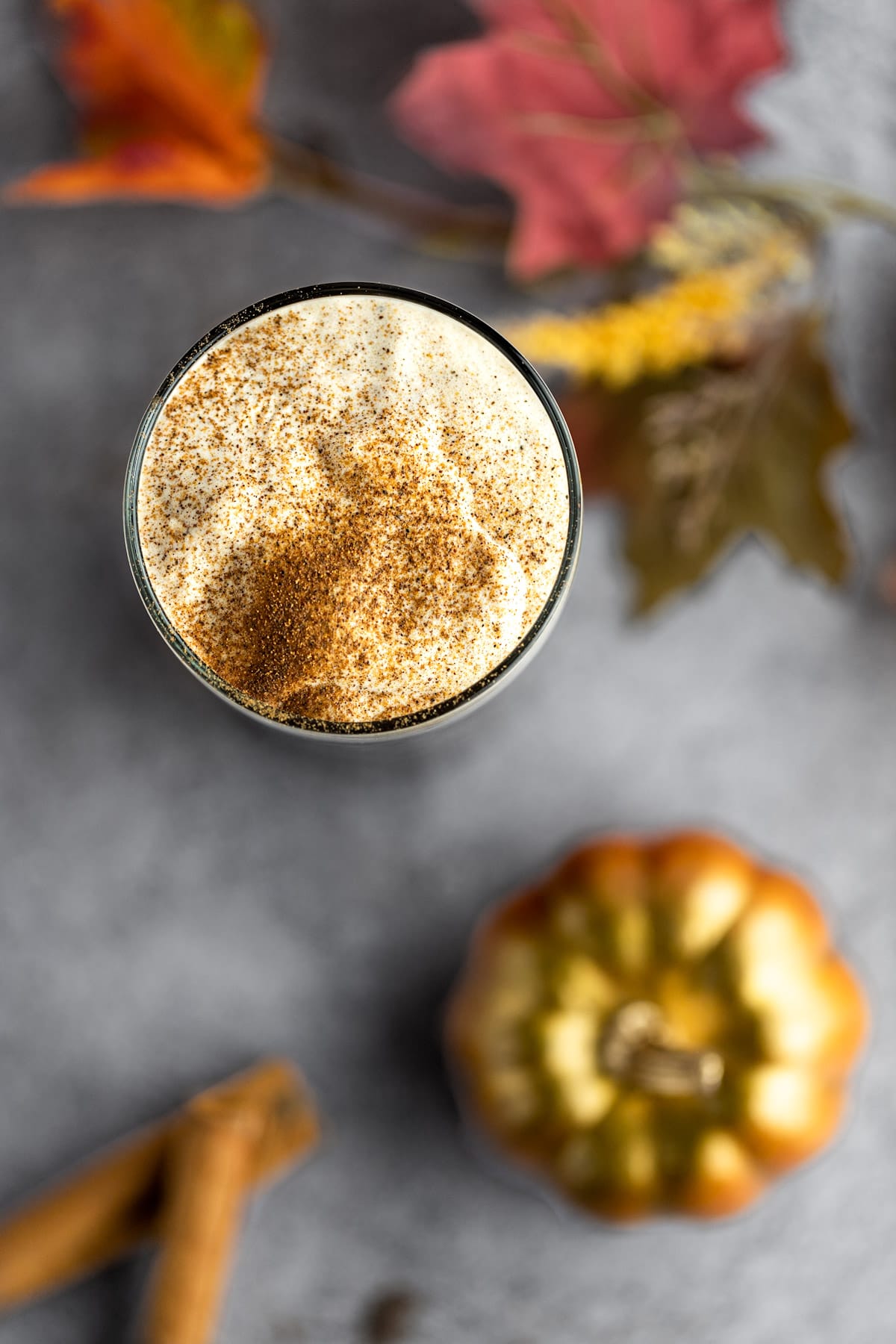 Overhead photo of pumpkin cold foam, surrounded by cinnamon sticks, a gold pumpkin and fall leaves.