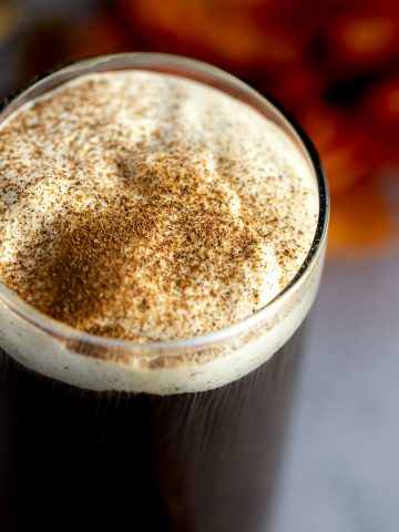 Pumpkin cold foam sprinkled with pumpkin spice, sitting on top of a glass of black coffee.
