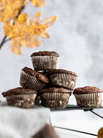 A stack of pumpkin protein muffins on a black wire rack, with a vase of golden leaves in the background.