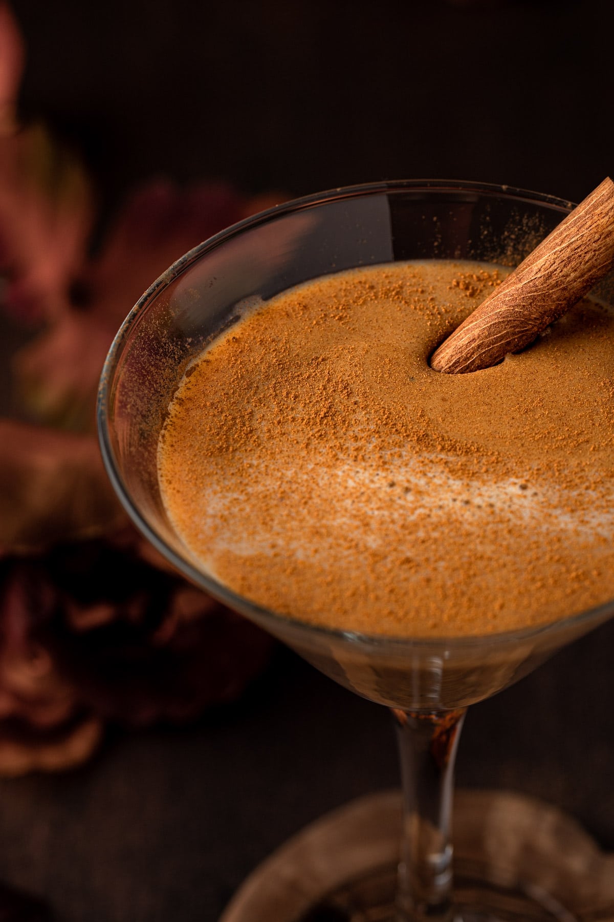 RumChata pumpkin martini garnished with pumpkin pie spice and a cinnamon stick, sitting on a wooden table.