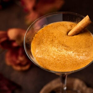 A pumpkin RumChata martini sprinkled with pumpkin pie spice on top and garnished with a cinnamon stick.