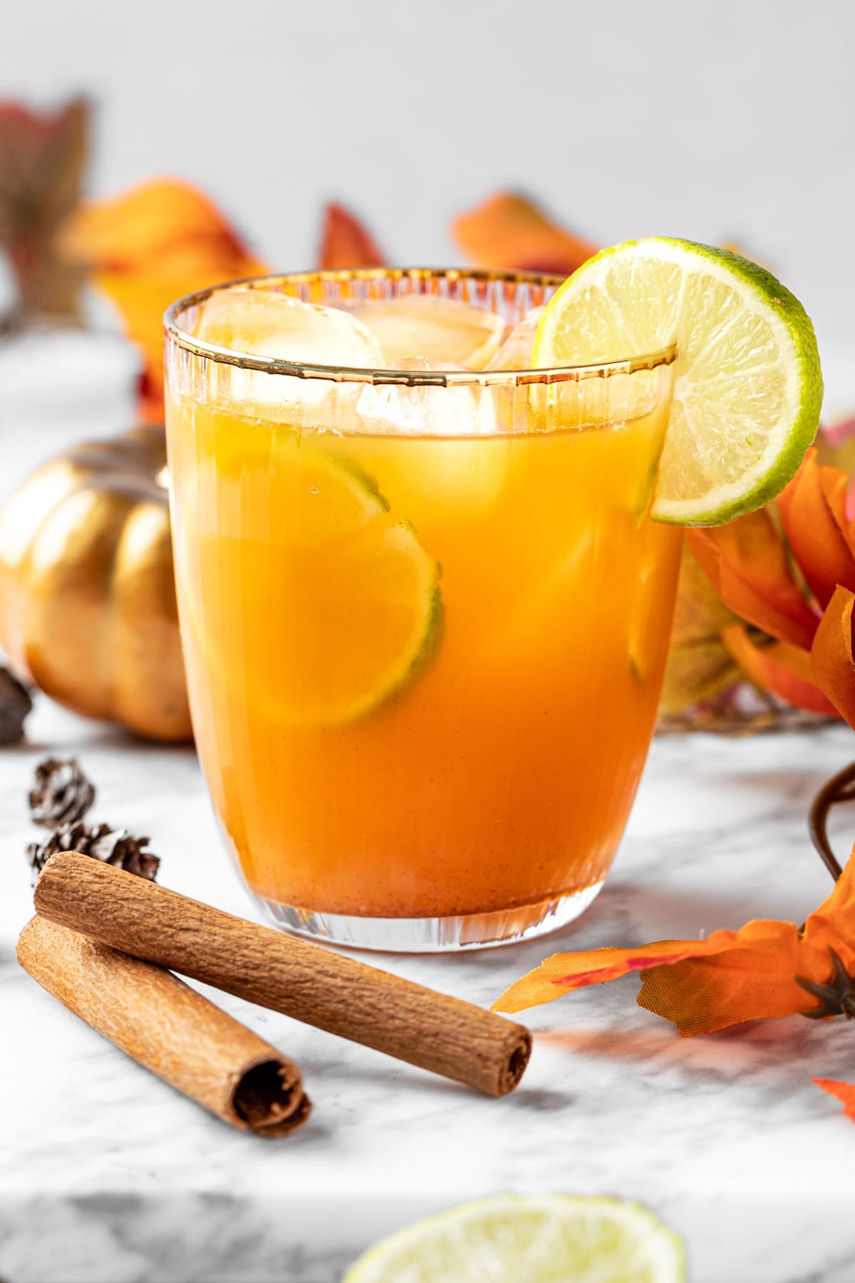 A pumpkin spice margarita garnished with lime, with fall leaves in the background.