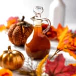 A bottle of pumpkin spice syrup surrounded by fall leaves and pumpkins.