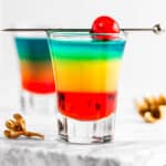 Rainbow shots with red, yellow and blue layers, garnished with a maraschino cherry.