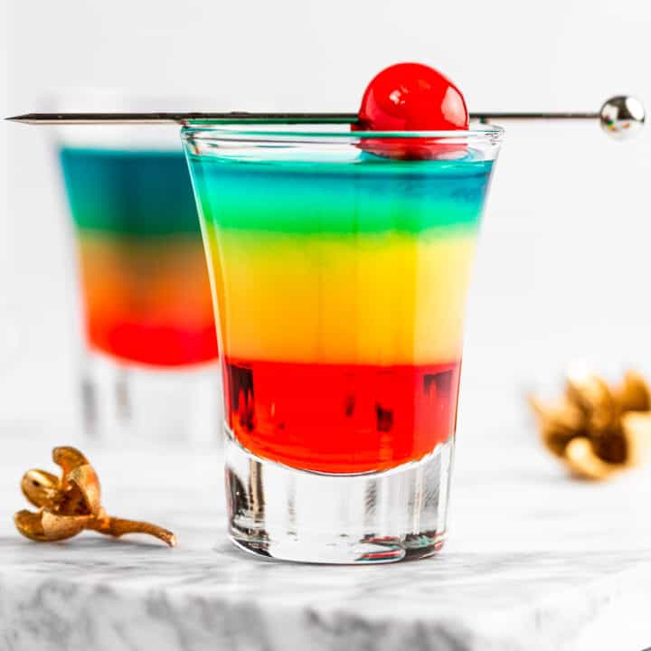 Rainbow shots with red, yellow and blue layers, garnished with a maraschino cherry.