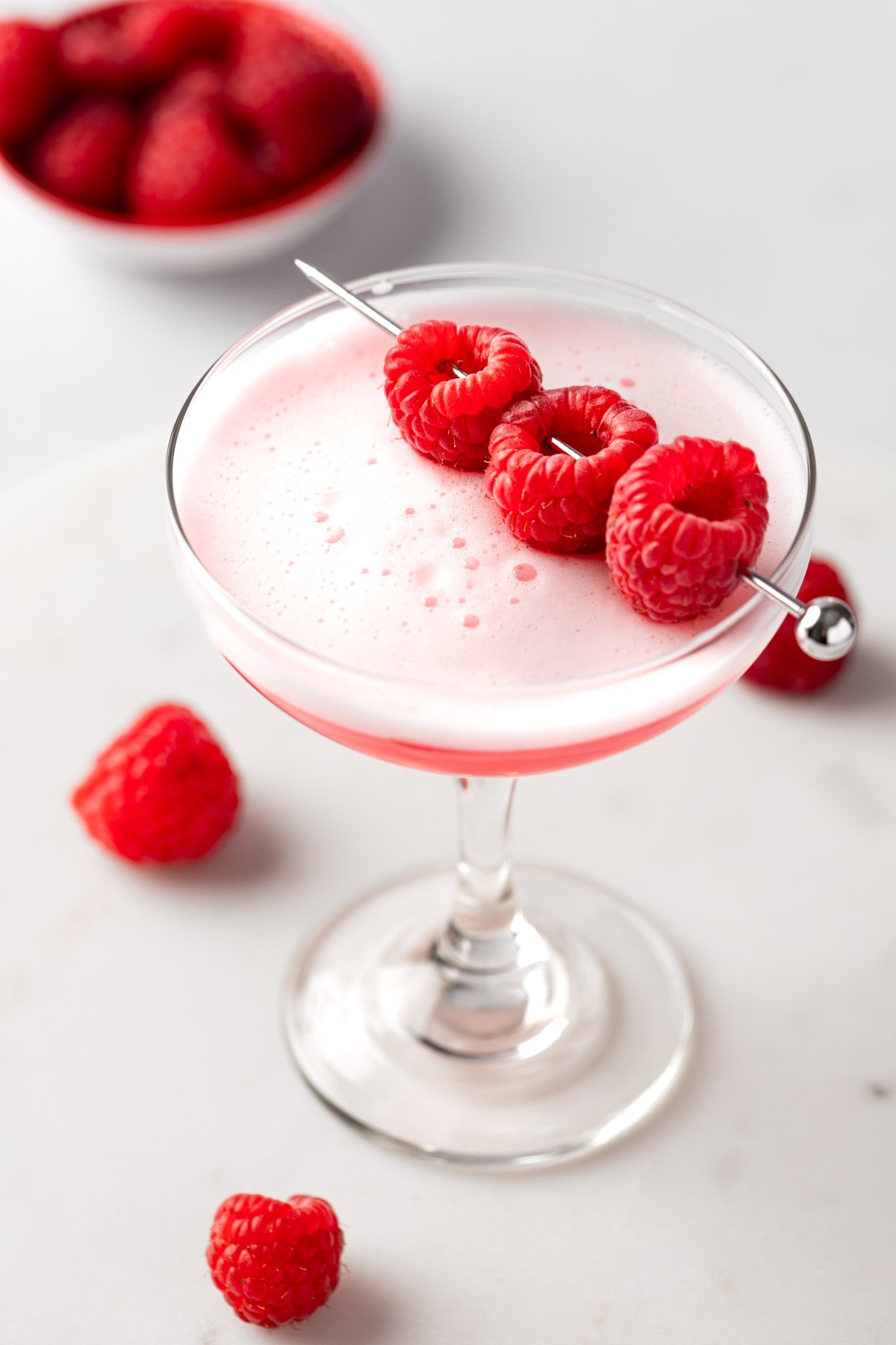 A raspberry gin sour served in a coupe glass, garnished with fresh raspberries.