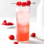 A raspberry gin fizz served in a Collins glass, garnished with fresh raspberries.