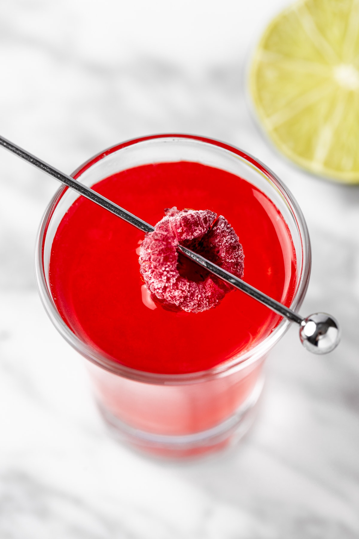 Overhead view of a raspberry kamikaze shot garnished with a raspberry.