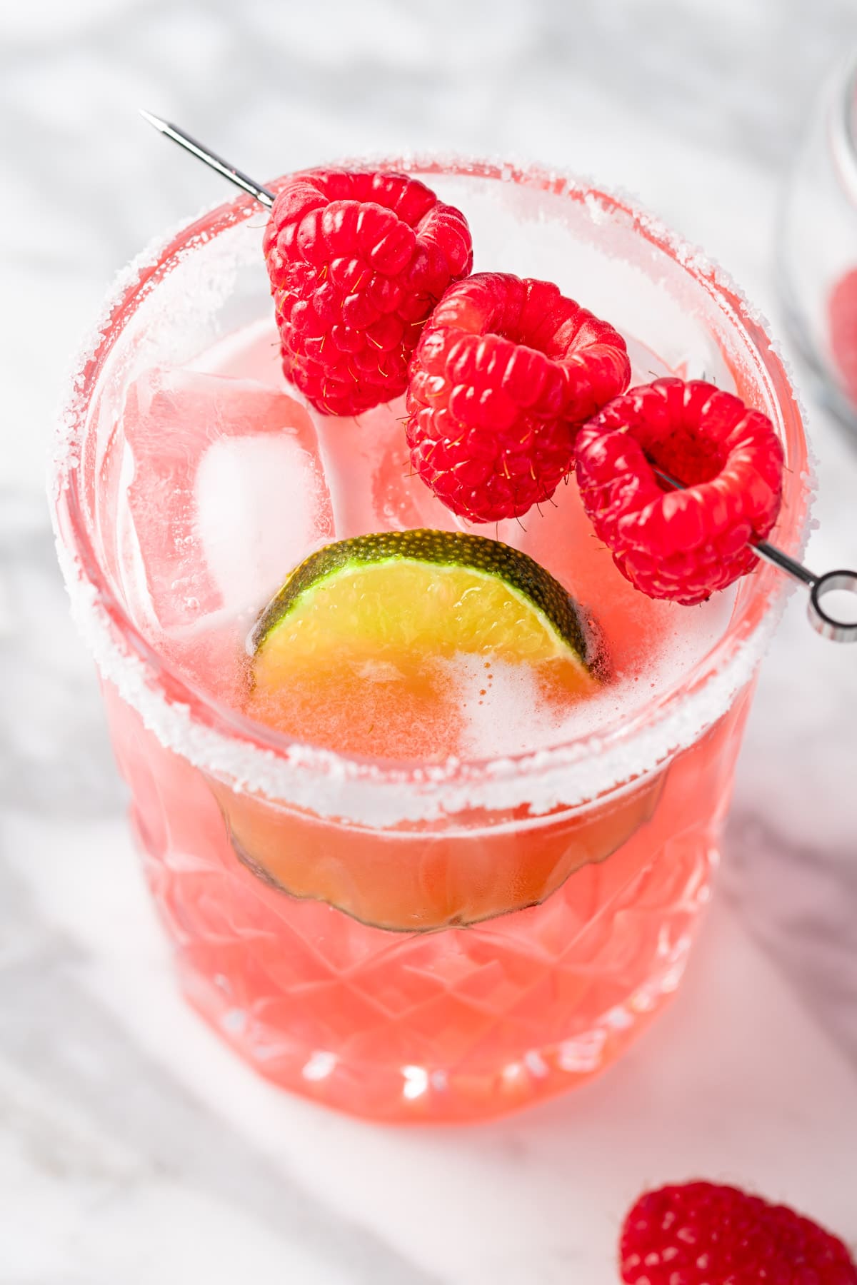 A raspberry margarita on the rocks garnished with fresh raspberries and a lime slice.