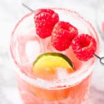 A raspberry margarita on the rocks garnished with fresh raspberries and a lime slice.