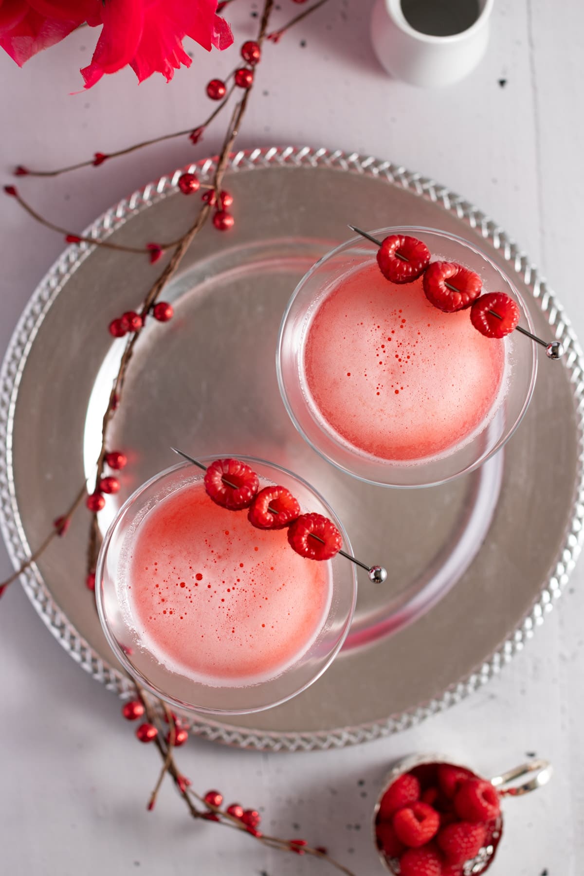 Overhead view of two cocktails on a silver plate, with a red berry garland on the table as decoration.